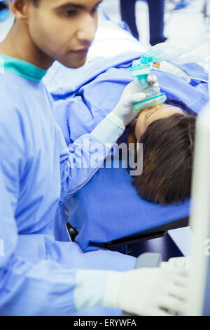 Anestesista tenendo le maschere di ossigeno oltre il viso del paziente in sala operatoria Foto Stock