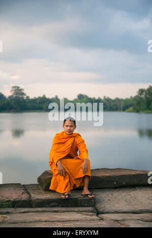 SIEM REAP, Cambogia - 30 ottobre 2014: il Principiante monaco buddista in veste arancione si trova lungo il fossato vicino all'entrata di Angkor Wat. Foto Stock