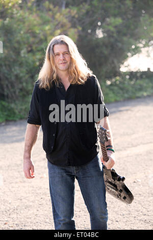 Con i capelli lunghi uomo con una chitarra a camminare su una strada Foto Stock