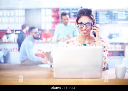 Imprenditrice utilizzando laptop e parlando al cellulare in cafe Foto Stock