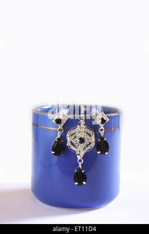 Orecchini appendere su blu tazza da caffè su sfondo bianco Foto Stock