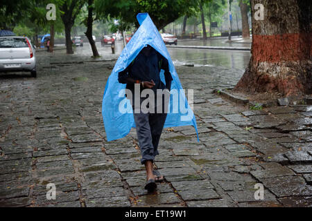 Uomo che cammina in Rainy Street coperto con una busta di plastica come ombrello signor# 364 Foto Stock