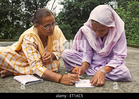 Insegnamento di volontariato old Lady per scrivere programma di alfabetizzazione per adulti socio iniziativa economica avviato da ONG Organizzazione Chinmaya Foto Stock