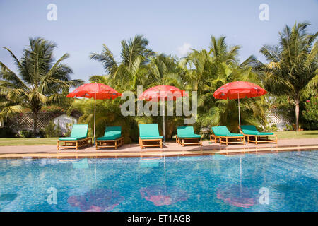 Tre colori rosso ombrellone vicino alla piscina blu verde acqua palme e cielo blu ; Palolem beach ; Goa ; India Foto Stock