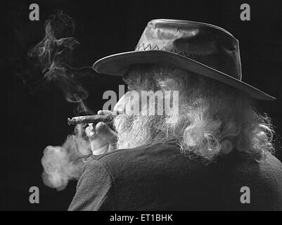 vecchio che indossa un cappello che fuma sigaro barba bianca sfondo nero e bianco nero scatto studio Foto Stock