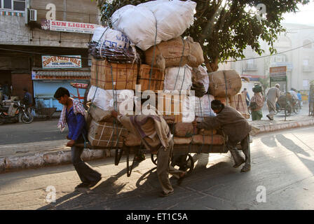 Uomini che tirano carretto a spinta con bagaglio pesante nella zona di Chandni Chowk ; Delhi ; India Foto Stock