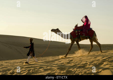 L'uomo trascinando cammello con donna seduta su di esso duna di sabbia Jaisalmer Rajasthan India Asia MR # 704 Foto Stock