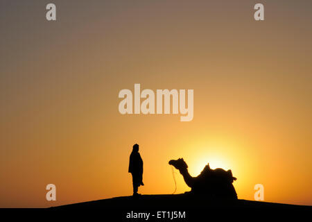 Sunrise glorioso uomo con cammello sulle dune di sabbia ; Jaisalmer ; Rajasthan ; India Foto Stock