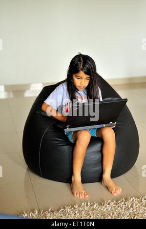 Ragazza bambino che lavora sul computer portatile seduto su borsetta MR#556 Foto Stock