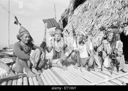 Notte uomini tribali seduti di fronte a casa battendo albero tronco seduto su piattaforma di bambù ; Arunachal Pradesh ; India ; Asia ; vecchio vintage 1900 quadro Foto Stock