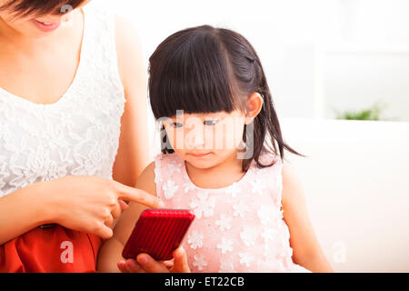 La madre e la bambina utilizza lo smartphone insieme sul divano Foto Stock