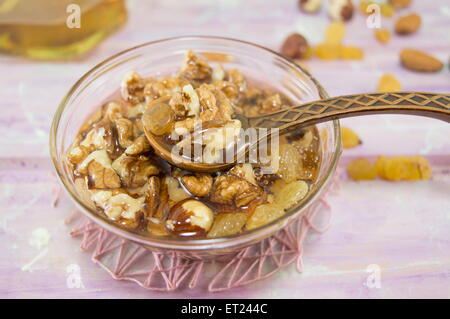 Noci nocciole e miele in un piatto di vetro con un vintage cucchiaio di legno su una tovaglia rosa Foto Stock
