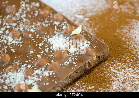 Il cioccolato con le nocciole su una superficie cosparsa di cacao e polvere di noce di cocco Foto Stock