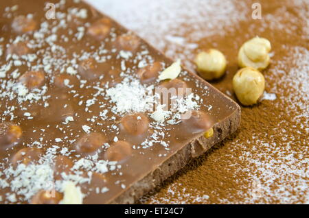 Il cioccolato con le nocciole su una superficie cosparsa di cacao e polvere di noce di cocco Foto Stock