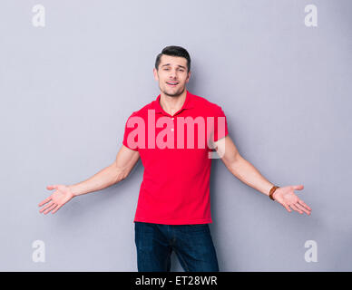 Bel giovane uomo che ti accoglie con le sue braccia aperte su sfondo grigio Foto Stock