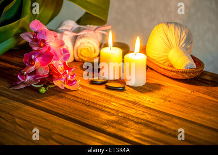 Spa concept di rosa fiori di orchidea, tailandese alle erbe comprimere le sfere nel cestello, asciugamani, pietre zen e candele su sfondo di legno, cl Foto Stock