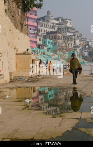 Un uomo cammina lungo i ghats sulle rive del Gange a Varanasi Foto Stock