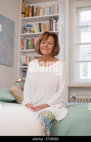 Senior donna seduta sul letto e sorridente, Monaco di Baviera, Germania Foto Stock