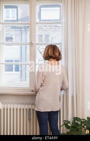 Vista posteriore della donna senior di guardare attraverso una finestra, Monaco di Baviera, Germania Foto Stock