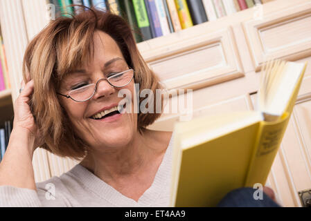 Senior donna durante la lettura di fronte a scaffale, Monaco di Baviera, Germania Foto Stock