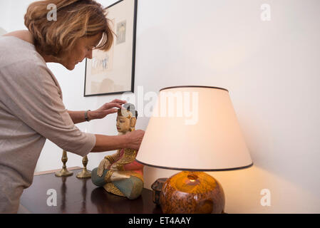 Senior donna tocca la statua di Buddha nella posizione del loto, lampada in primo piano, Monaco di Baviera, Germania Foto Stock