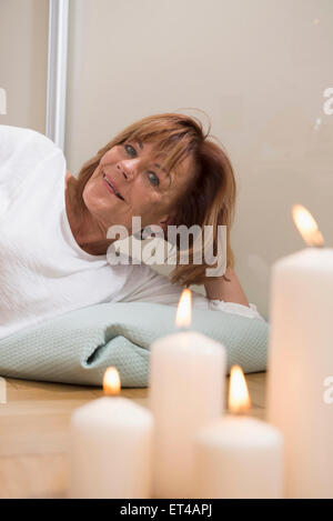 Senior donna sdraiata con cuscino sul piano, candele accese in primo piano, Monaco di Baviera, Germania Foto Stock