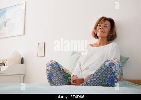 Senior donna seduta sul letto e pensare, Monaco di Baviera, Germania Foto Stock