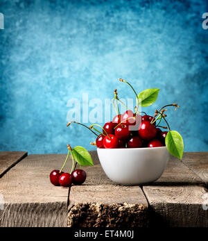 Ciliege rosse nella piastra su una tavola di legno Foto Stock