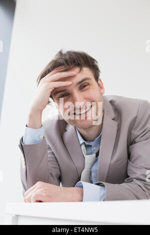 Uomo d'affari sorridente appoggiato alla scrivania in ufficio, Lipsia, Sassonia, Germania Foto Stock