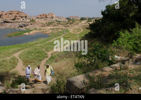 Tre uomini a piedi attraversata la paesaggio all'antica città di Hampi, India Foto Stock