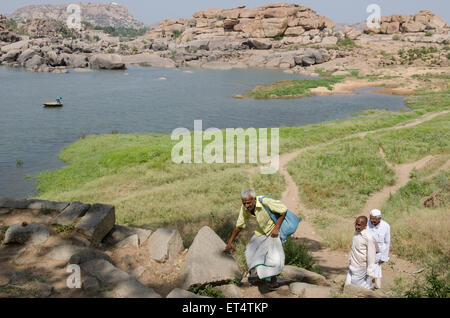 Tre uomini a piedi attraversata la paesaggio all'antica città di Hampi, India Foto Stock