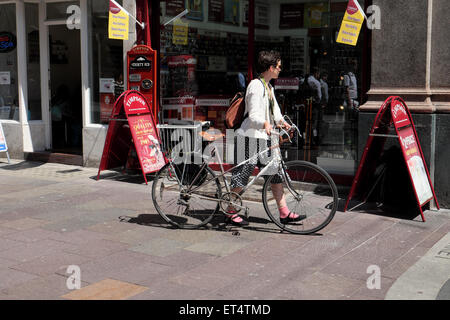 Ciclista femmina con retro bike e Sella in cuoio camminando sul marciapiede lungo St Marys Street Cardiff Wales UK KATHY DEWITT Foto Stock