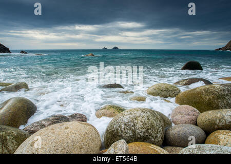 Boulder coperta spiaggia a Porth Nanven alla fine della valle di culla con il Brisons all'orizzonte, Cornwall Inghilterra UK Europa Foto Stock