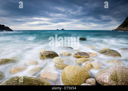 Boulder coperta spiaggia a Porth Nanven alla fine della valle di culla con il Brisons all'orizzonte, Cornwall Inghilterra UK Europa Foto Stock