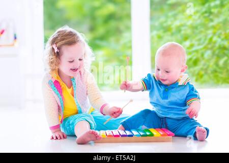 Due bambini piccoli - molto carino curly toddler girl e una divertente baby boy, fratello e sorella di riproduzione di musica con xilofono colorato Foto Stock