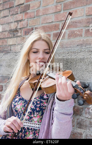 Caucasian ragazza adolescente suona il violino di fronte a un muro di mattoni, Monaco di Baviera, Germania Foto Stock