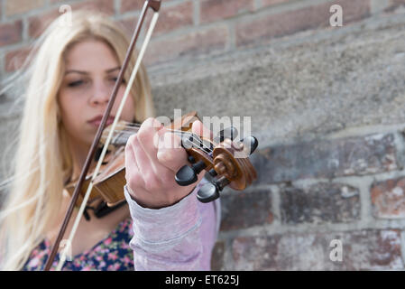 Caucasian ragazza adolescente suona il violino di fronte a un muro di mattoni, Monaco di Baviera, Germania Foto Stock