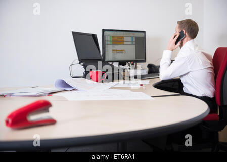 Uomo che lavora in ufficio e parlando al telefono cellulare, Monaco di Baviera, Germania Foto Stock