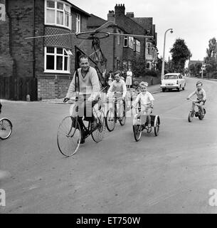 Signor Clifford Davis di strada di Leeds Wakefield, tenta di eseguire la sua macchina volante realizzato da bit di vecchi cicli di pedale. Dopo di lui in giù per la strada sulle loro moto sono vicini i bambini, West Yorkshire, 25 giugno 1965. Foto Stock