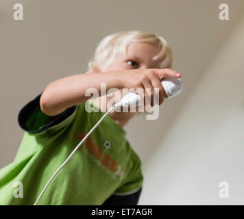 Ragazzo di 7 anni in casa giocare con il Nintendo Wii gioco per computer con Nintendo game controller (Nunchuk) nella sua mano. Foto Stock