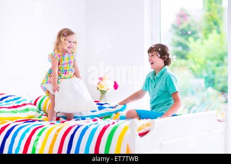 Due bambini, felici di ridere boy e carino curly bambina divertendosi alla lotta di cuscini di piume nel saltare per aria Foto Stock