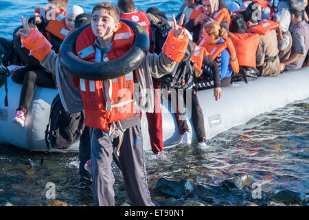 Giovane rifugiato siriano segnali la vittoria come la sua zattera attraversa in modo sicuro dalla Turchia alla Grecia e terre sulla riva greca. Foto Stock