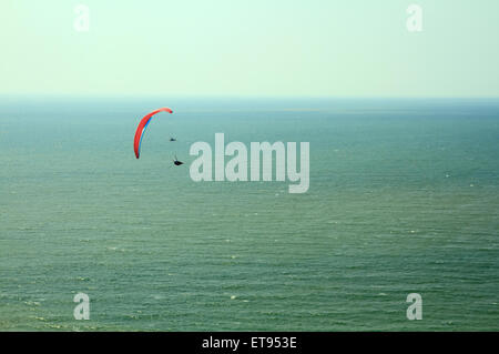 Red parapendio vola nel cielo blu sull'oceano. Foto Stock