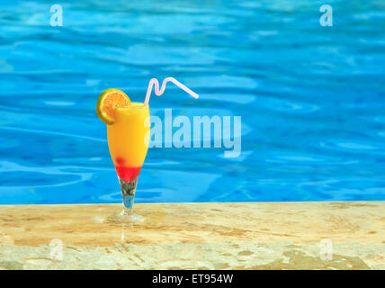 Bicchiere di succo orage è sul bordo della piscina Foto Stock