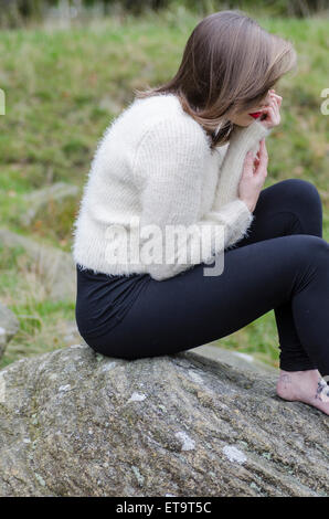 Giovane donna sat su rocce Foto Stock