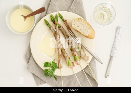 Asparagi verdi grigliati spiedini avvolto con pancetta servito con salsa hollandaise, vino bianco e baguette Foto Stock