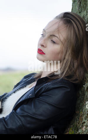 Triste giovane donna appoggiata contro un albero in campagna Foto Stock