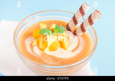 Peach dessert (mousse) con yogurt, waffle rotoli e menta close up su sfondo blu Foto Stock