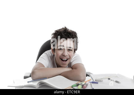 Ragazzo ride appoggiata con le braccia conserte sul libro bianco, sul lavoro a domicilio: libri,copybooks e matite Foto Stock