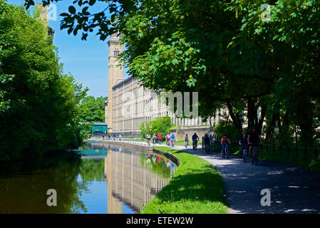 I ciclisti su strada alzaia di Leeds e Liverpool Canal e il sale's Mill, Saltaire, West Yorkshire, Inghilterra, Regno Unito Foto Stock